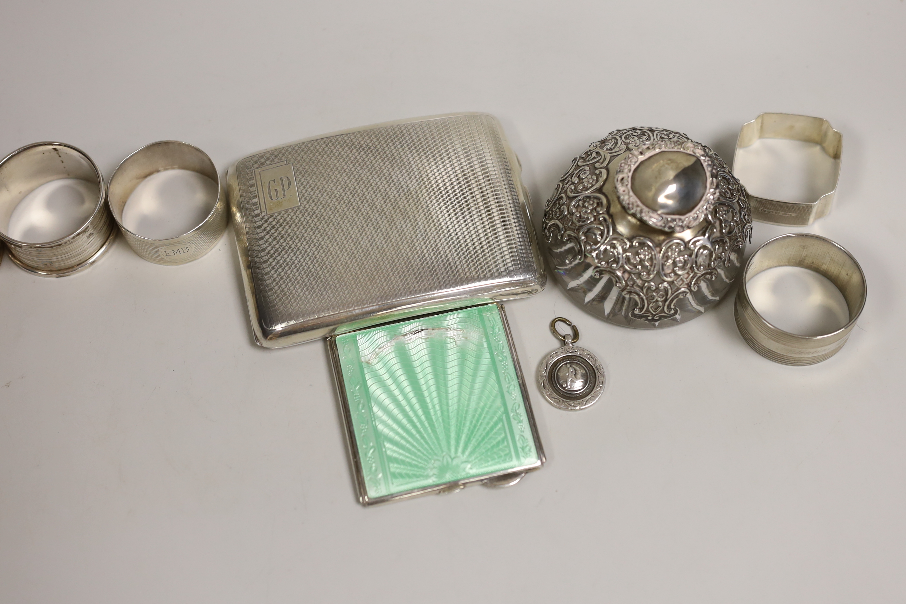 A quantity of mixed silver ware including a cigarette case and enamelled compact (a.f.), a mounted glass inkwell, five napkin rings, (one plated), a brooch and a Fattorini & Sons football pendant.